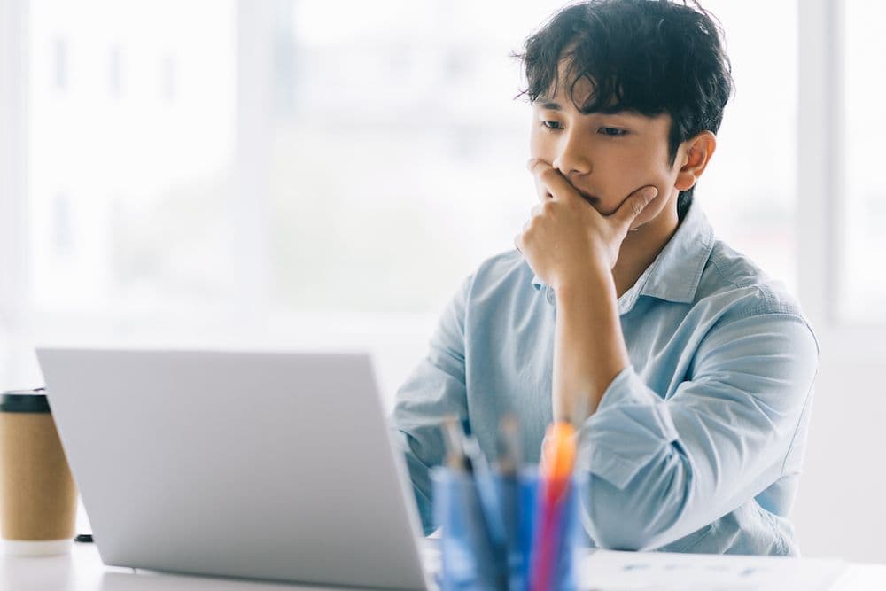 persona sentada con el ceño fruncido, se sujeta la boca con ansiedad mientras espera que finalice una tarea de procesamiento de datos en su computadora portátil