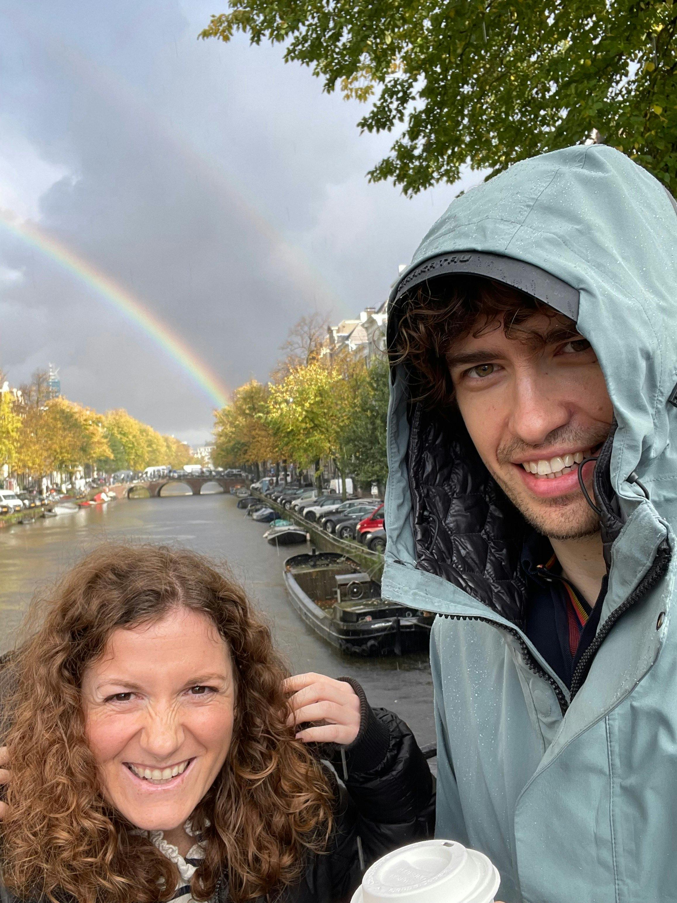 Two colleagues in front of a canal in Amsterdam. In the background is a double rainbow.
