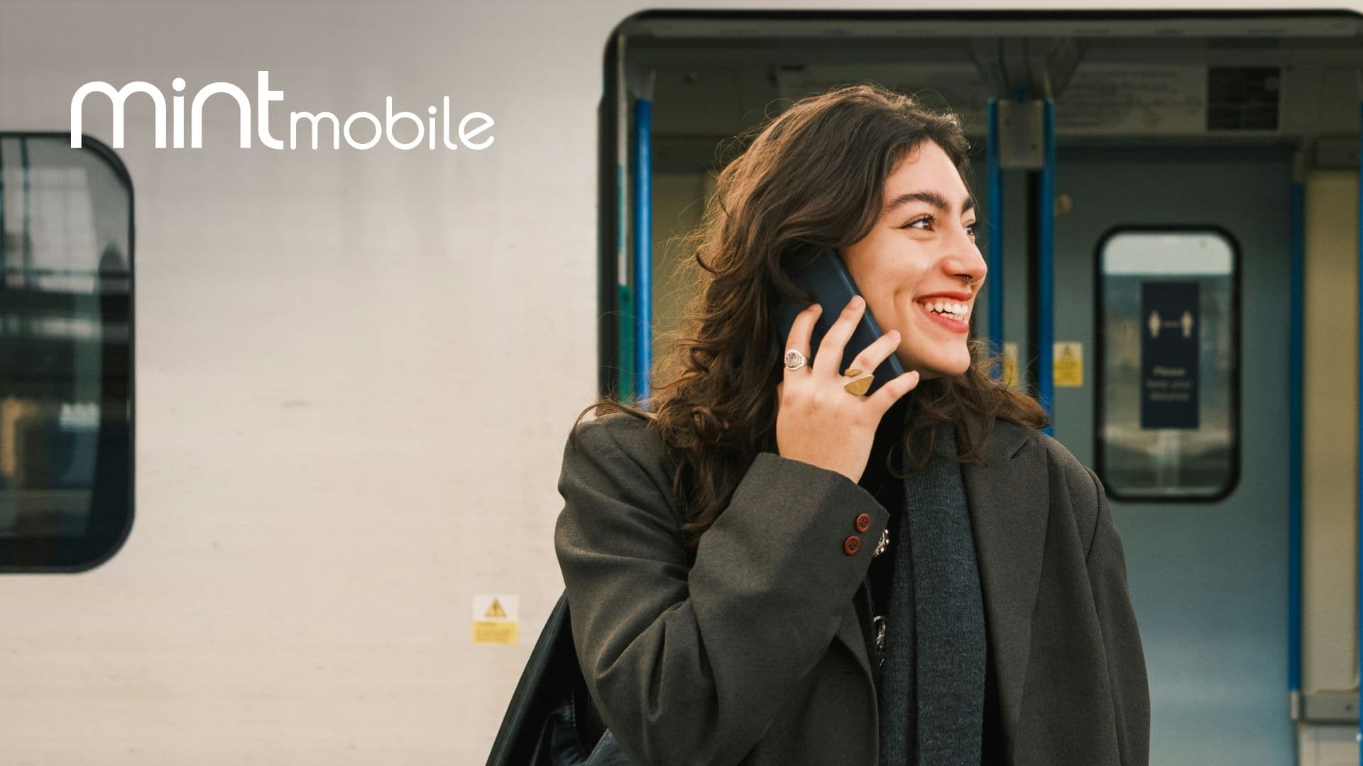 A woman talks on a cellular phone in front of a train, with the mint mobile logo in the top left corner.