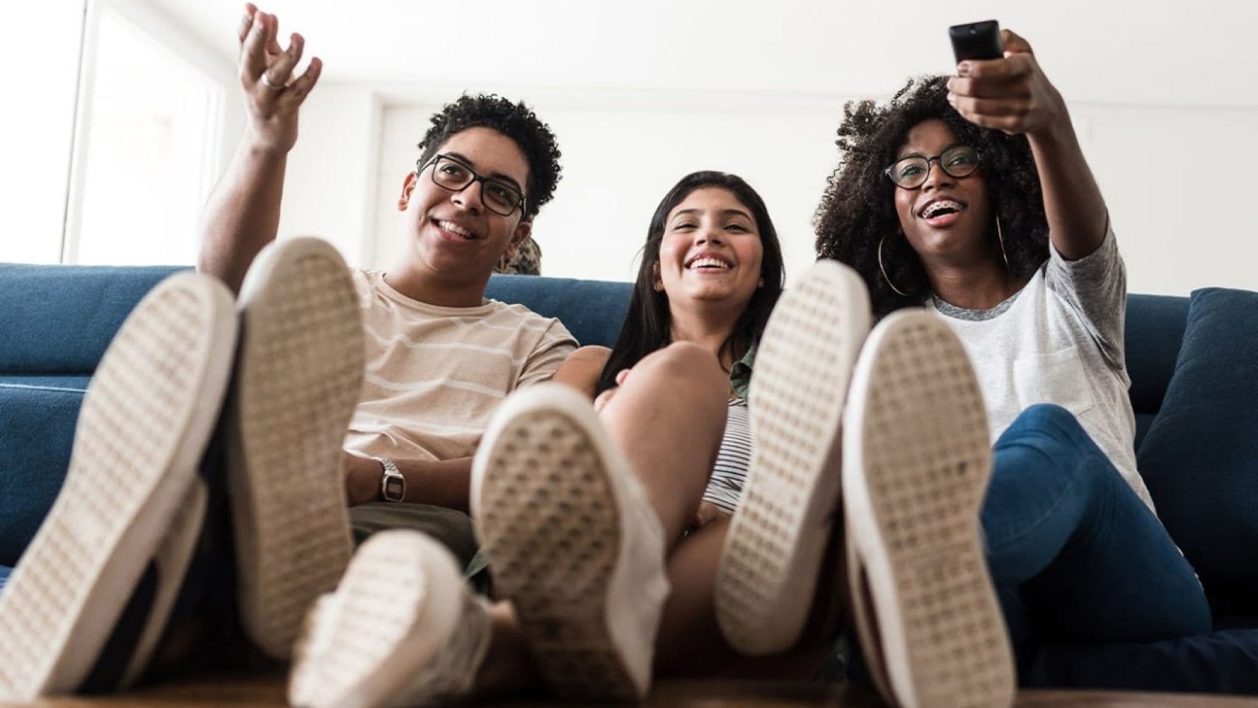 Three people seated on the sofa watching, one holding a remote