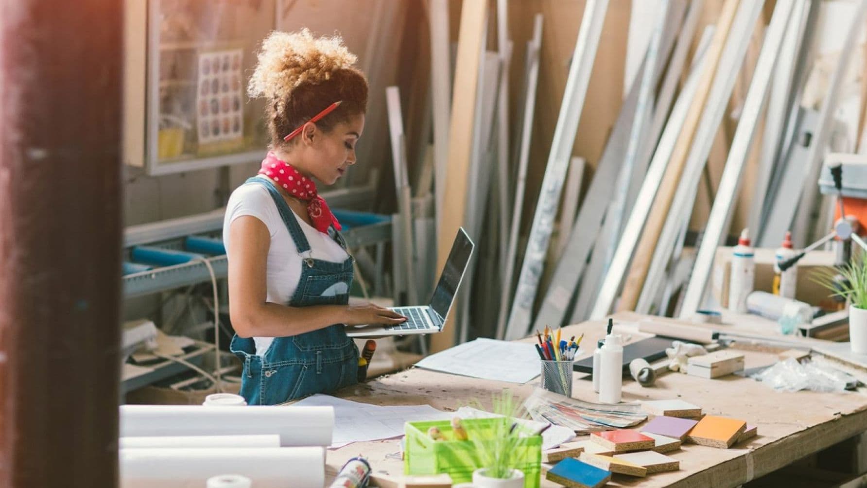 Focused lady in the workshop with a pencil tucked behind her ear as she deftly operates her laptop