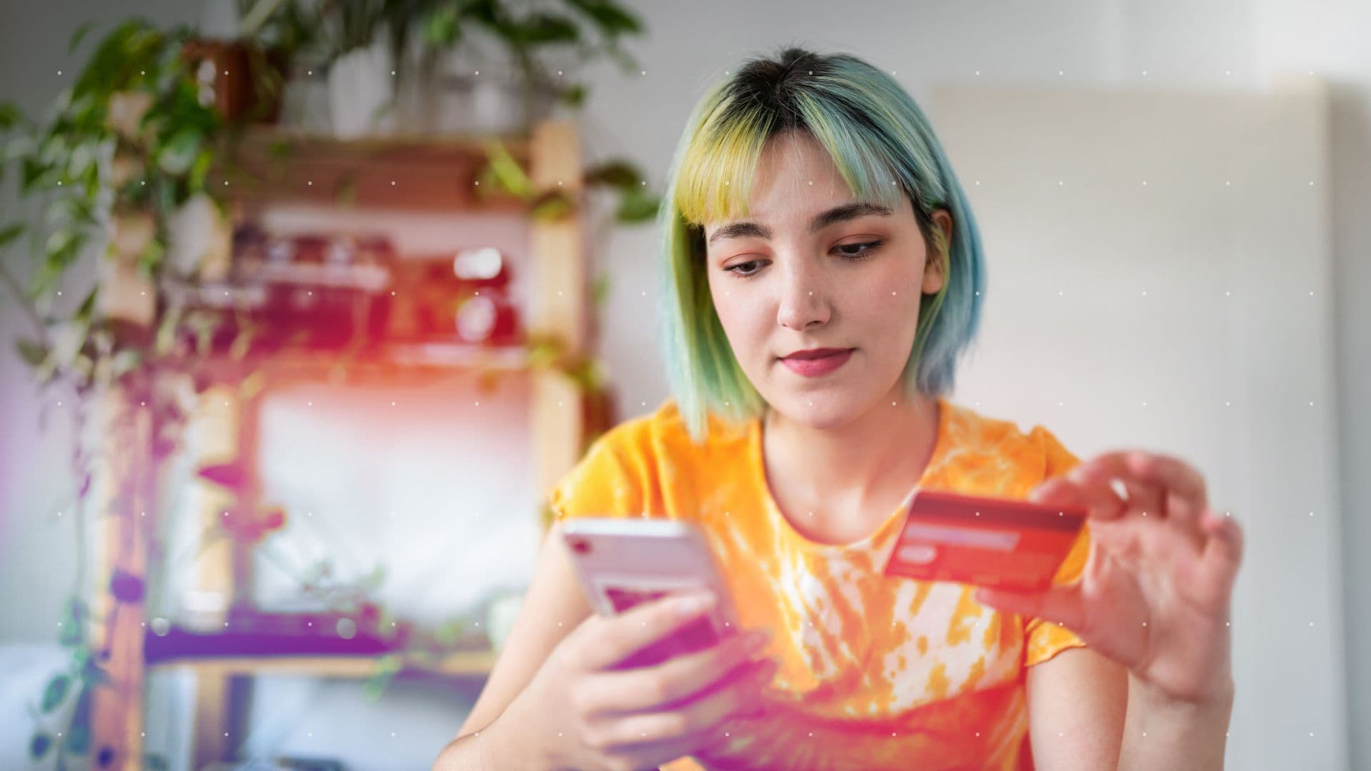 A young woman with colorful hair compares her phone screen against a credit card while shopping online