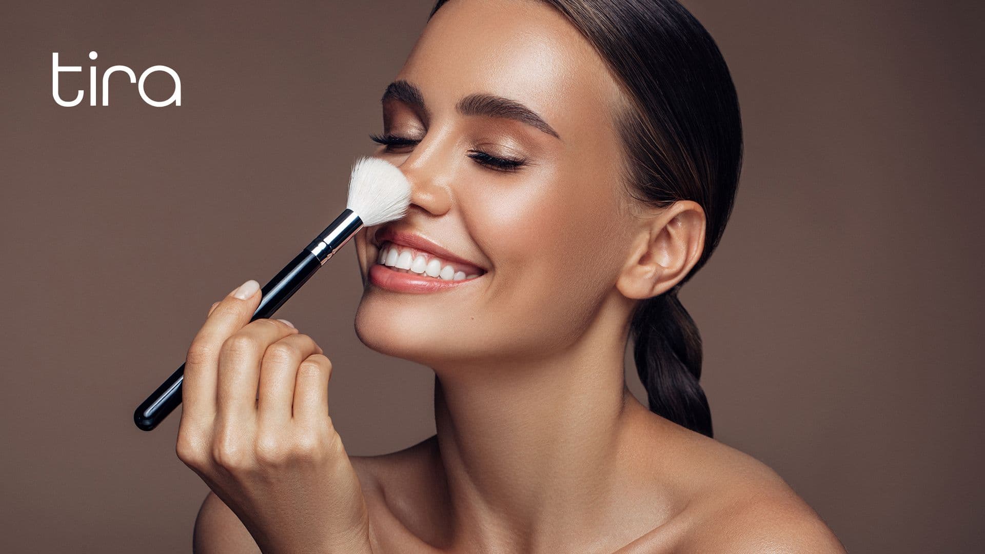 A smiling woman uses a makeup brush, suggesting the kind of customer Tira cultivates.